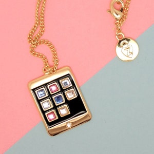 May include: A gold chain necklace with a black and gold phone charm. The phone charm has a black face with a grid of colorful rhinestones.