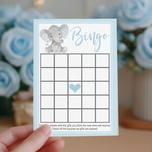 May include: A baby shower Bingo card with a light blue border and a cartoon elephant illustration. The word "Bingo" is written in cursive. The card has a grid of squares with a heart in the center. Text at the bottom instructs players to fill in blanks.