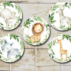May include: Five round cake toppers with watercolor illustrations of jungle animals. The animals are a giraffe, zebra, rhino, lion, and elephant. Each animal is surrounded by green leaves and a white background.