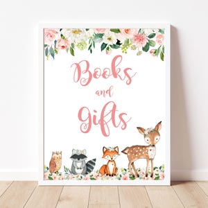 May include: A framed sign with the words "Books and Gifts" in pink script, surrounded by floral arrangements. The bottom of the sign features illustrations of an owl, raccoon, fox, and deer, all adorned with floral crowns.