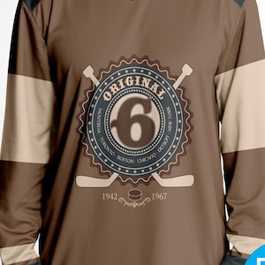 May include: A brown and beige long-sleeved hockey jersey with a vintage-style logo featuring the number "6" and the word "ORIGINAL" in a circle. The logo also includes the cities "Montreal, Toronto, Boston, Chicago, Detroit, New York" and the years "1942 - 1967".