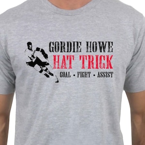 May include: A grey t-shirt with a black and white image of a hockey player and the text "Gordie Howe Hat Trick Goal - Fight - Assist" printed on the front.