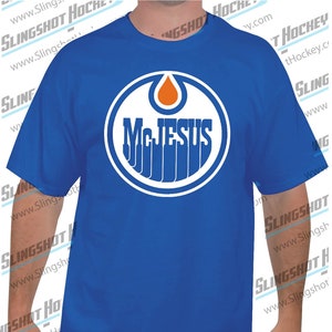 May include: A royal blue t-shirt with a white circular logo featuring a stylized flame and the text "McJESUS".