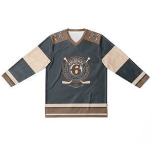 May include: A dark blue hockey jersey with brown and beige accents. The jersey has a large circular logo with the text "ORIGINAL" and the number "6" inside. The logo also includes the text "1942 - 1967".