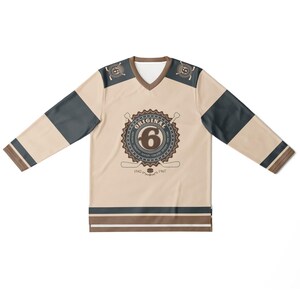 May include: A beige hockey jersey with brown and black stripes. The jersey has a large brown circle with the text "ORIGINAL" and the number "6" in the center. The text "1942" and "1967" are below the circle.