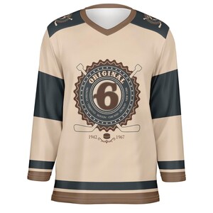 May include: A beige hockey jersey with brown and black stripes. The jersey features a brown circular logo with the text "ORIGINAL" and the number "6" inside. The logo also includes the text "MONTREAL, TORONTO, BOSTON, CHICAGO, DETROIT, NEW YORK" around the number. The text "1942" and "1967" are below the logo.