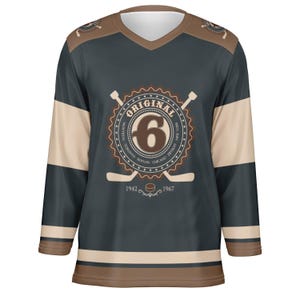 May include: A dark blue hockey jersey with a white and brown striped pattern. The jersey features a large circular logo with the word "ORIGINAL" and the number "6" in the center. The logo is surrounded by the names of six cities: Montreal, Toronto, Boston, Chicago, Detroit, and New York. The jersey also has two crossed hockey sticks and a puck with the years 1942 and 1967.