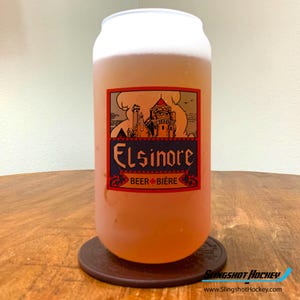 May include: A frosted glass beer can with a red, white, and blue label that says "Elsinore Beer Biere". The label features a drawing of a castle.