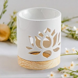 Può includere: Diffusore di oli essenziali in ceramica bianca con un design a forma di fiore di loto traforato. Il diffusore ha una forma cilindrica con una base in legno. La parte superiore ha un'ampia apertura per olio e acqua. Accenti floreali sullo sfondo.