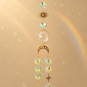 Può includere: Un acchiappasole sospeso con catena dorata, perline di cristallo sfaccettato iridescente, una sfera di cristallo trasparente in un anello d'oro, un ciondolo a forma di sole, un connettore a fasi lunari e una stella con una piccola luna.