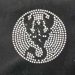 May include: A circular design composed of numerous small, white, circular rhinestones on a black background. The rhinestones are arranged to form a pattern, creating a sparkling effect. The design is centered and takes up a significant portion of the image.