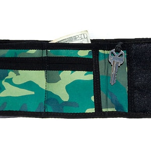 Puede incluir: Una cartera de camuflaje verde y negro con una llave adjunta.