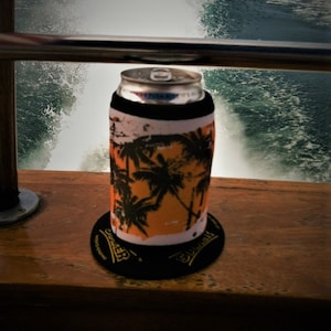 Puede incluir: Una lata de cerveza con una funda de enfriador con estampado de palmeras tropicales y un posavasos negro con la palabra "Brewer" impresa en amarillo.