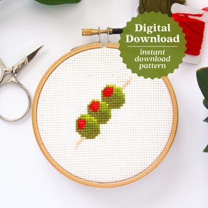 May include: A cross stitch pattern of green olives on a skewer, displayed in a wooden embroidery hoop. The pattern is ready to download.