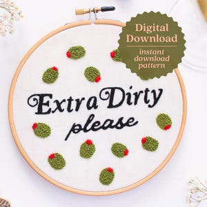 Puede incluir: Un aro de bordado blanco con un diseño de aceitunas verdes y rojas y el texto "Extra Dirty Please".