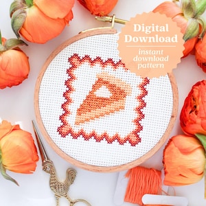 May include: A cross-stitch pattern of a slice of pumpkin pie in an embroidery hoop. The hoop is surrounded by orange flowers and embroidery floss. The text "Digital Download instant download pattern" is on a peach-colored circle.