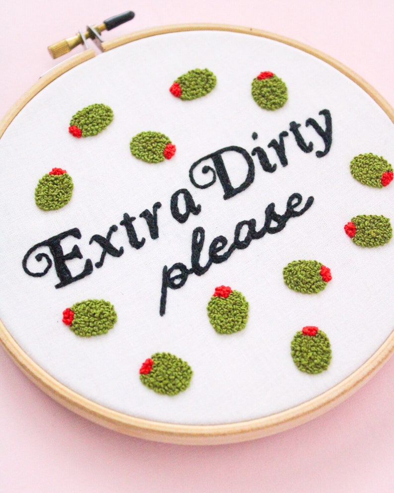 May include: Embroidered hoop art with the text "Extra Dirty please" surrounded by green olives with red centers.