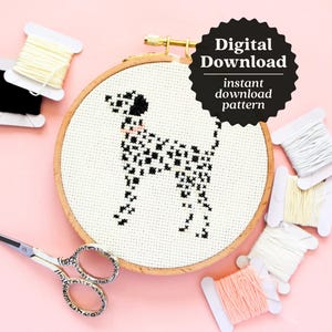 May include: A black and white cross-stitch pattern of a Dalmatian dog in a wooden embroidery hoop. The hoop is surrounded by spools of white embroidery floss on a pink background. The text "Digital Download" and "instant download pattern" is on a black circle.