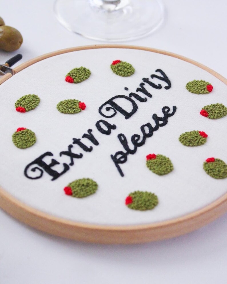 May include: Embroidered hoop with the text "Extra Dirty Please" in black cursive font. The hoop is decorated with green and red embroidered olives.