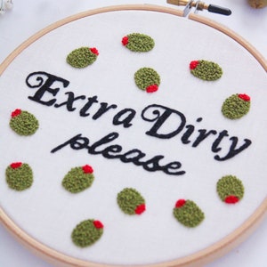 May include: Embroidered hoop art with the text "Extra Dirty please" and green olives with red centers.