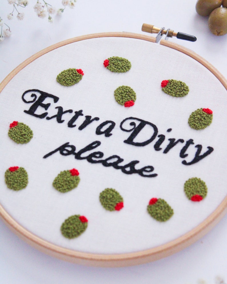 May include: Embroidered hoop art with the text "Extra Dirty please" and green olives with red centers.