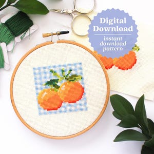 May include: A cross stitch pattern featuring two orange fruits with green leaves on a blue and white gingham background. The pattern is in a wooden embroidery hoop. The text "Digital Download" is on a blue starburst.