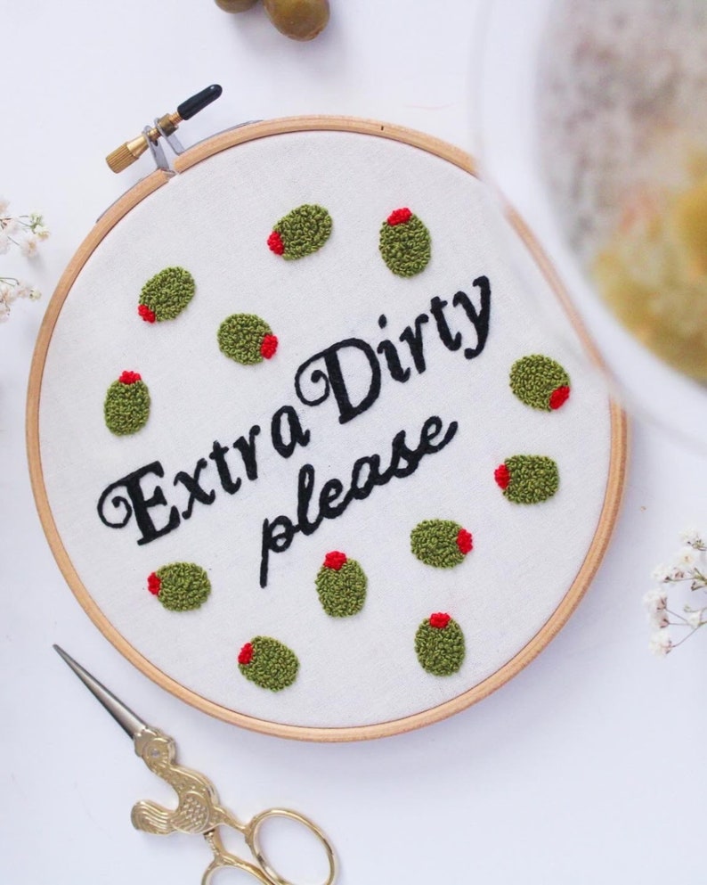 May include: Embroidered hoop art with the text "Extra Dirty please" and green olives with red centers.
