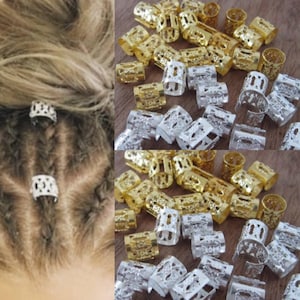 Puede incluir: Primer plano de una gran cantidad de cuentas para el cabello de metal dorado y plateado. Las cuentas tienen forma de cilindro con un diseño intrincado. Las cuentas se utilizan para decorar trenzas o rastas.