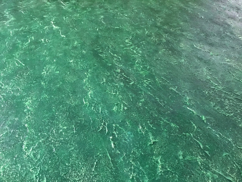 May include: A close-up of a textured green surface with a slightly mottled appearance. The surface has a rough, uneven texture.