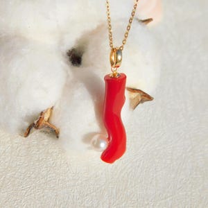 May include: A gold chain necklace with a red coral pendant and a white pearl accent.