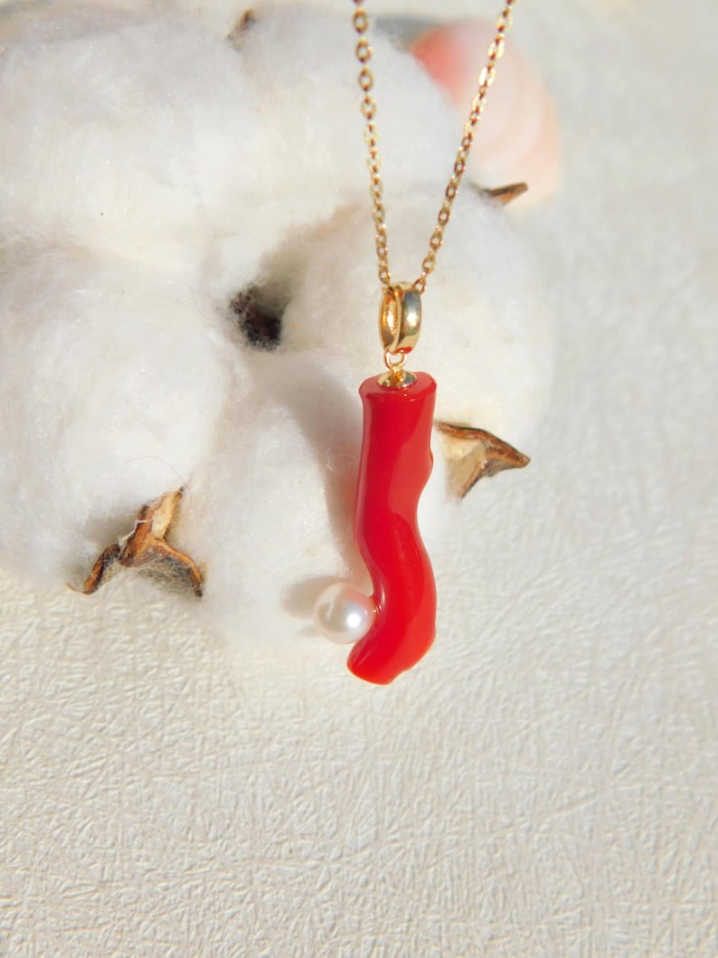 May include: A gold chain necklace with a red coral pendant and a white pearl accent.