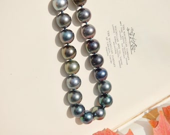 May include: A strand of dark blue and green iridescent pearls on a white surface with a red leaf.