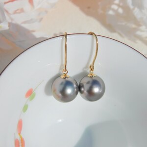 May include: A pair of gold earrings with gray pearl drops. The earrings are on a white background with a floral design.
