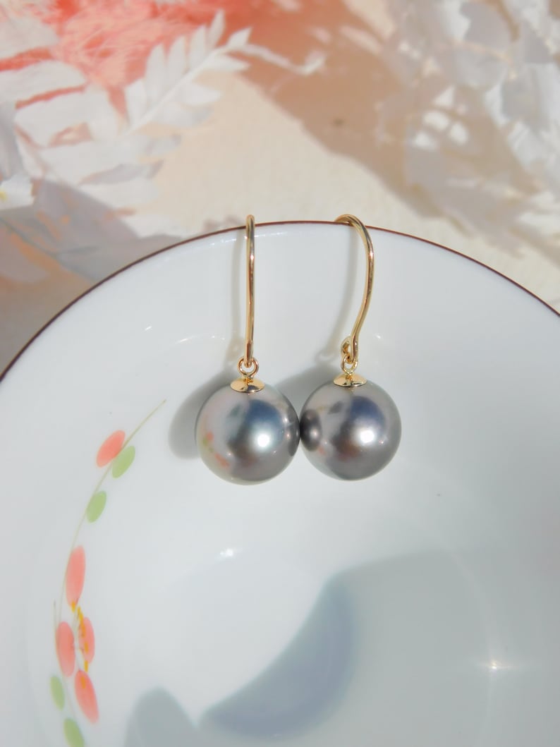 May include: A pair of gold earrings with gray pearl drops. The earrings are on a white background with a floral design.