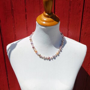 May include: A necklace made of pink, peach, and white pearls on a white mannequin against a red wooden background.