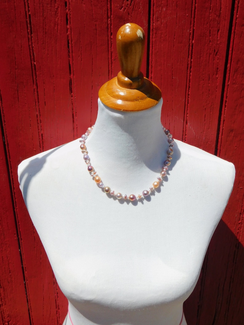 May include: A necklace made of pink, peach, and white pearls on a white mannequin against a red wooden background.