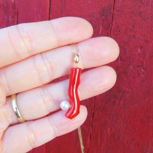 May include: A red coral pendant necklace with a white pearl accent. The necklace is on a gold chain.