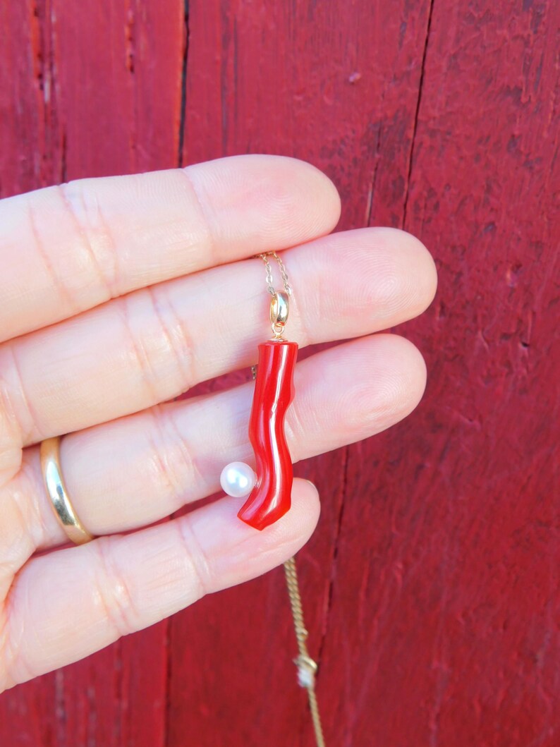 May include: A red coral pendant necklace with a white pearl accent. The necklace is on a gold chain.