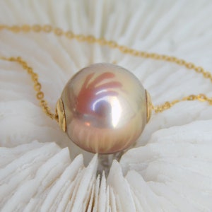 May include: A gold chain necklace with a large, iridescent pearl pendant. The pearl is a light pink colour with a subtle shimmer.