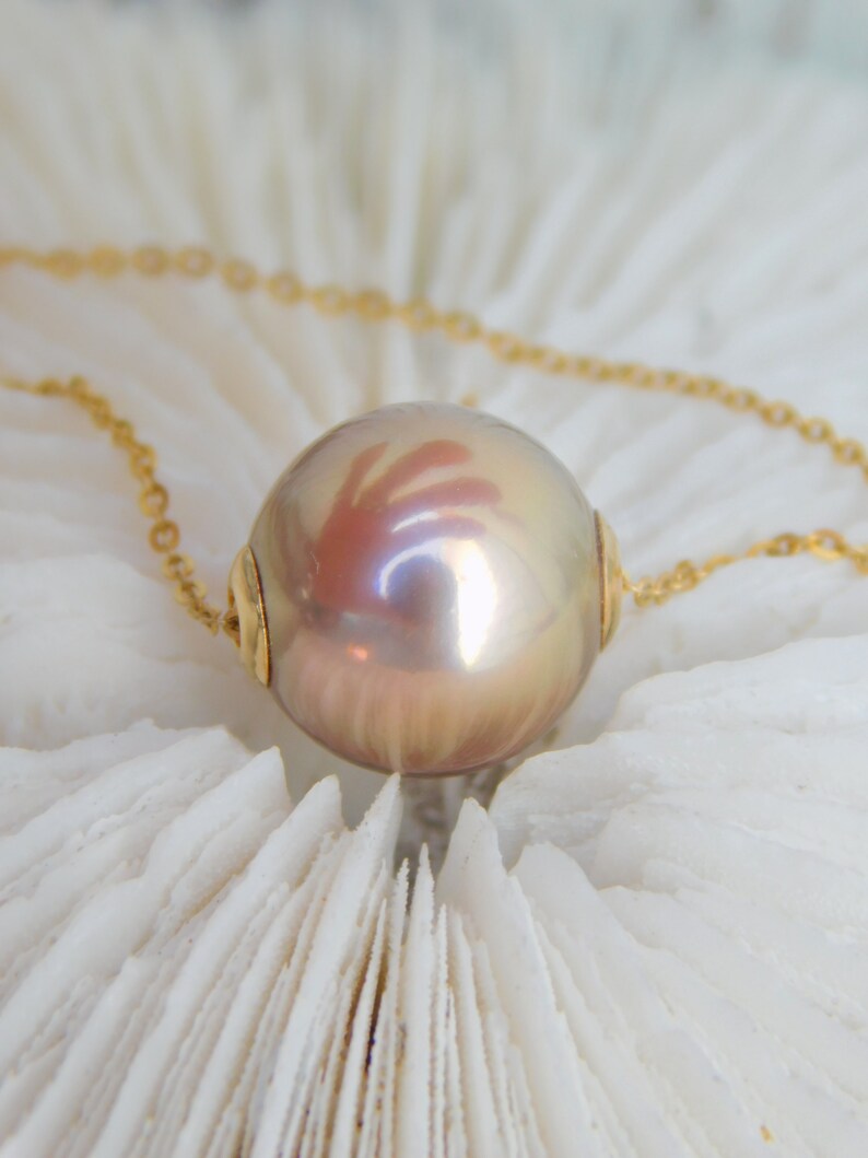 May include: A gold chain necklace with a large, iridescent pearl pendant. The pearl is a light pink colour with a subtle shimmer.