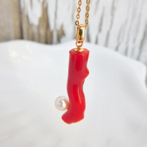 May include: A red coral pendant necklace with a white pearl accent. The necklace is made of gold chain.