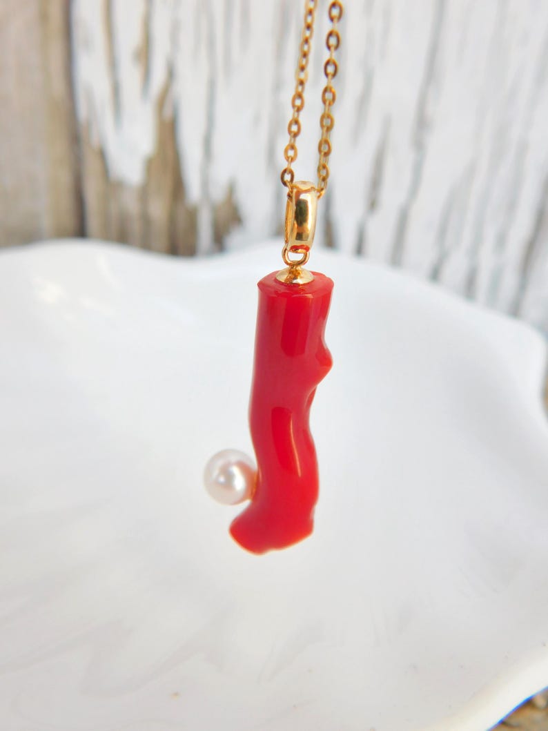 May include: A red coral pendant necklace with a white pearl accent. The necklace is made of gold chain.