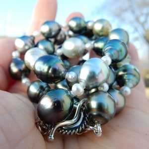 Op de afbeelding: Een ketting van zwarte en witte parels met een zilveren sluiting. De parels zijn in een los, vloeiend patroon gerangschikt.