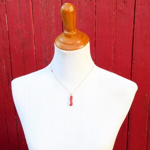 May include: A red coral pendant necklace on a gold chain, displayed on a white mannequin against a red wooden background.