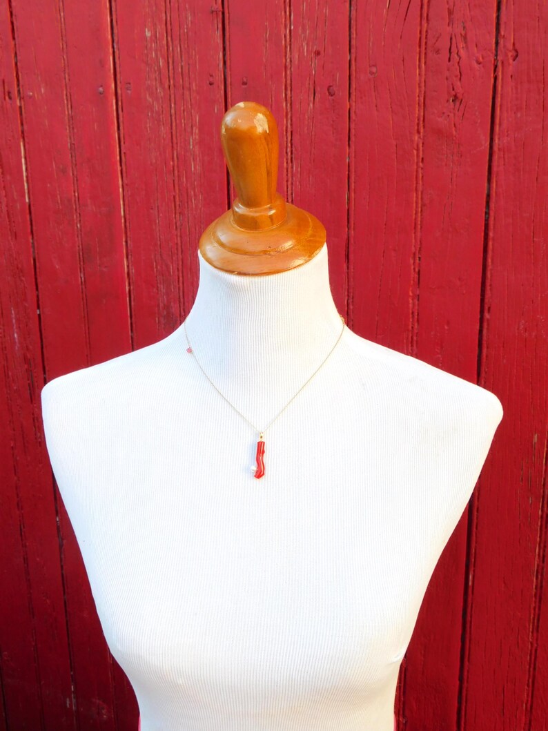 May include: A red coral pendant necklace on a gold chain, displayed on a white mannequin against a red wooden background.
