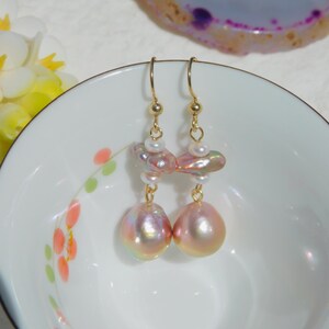 May include: A pair of gold dangle earrings with pink and white baroque pearls. The pearls are iridescent and have a pearlescent sheen.