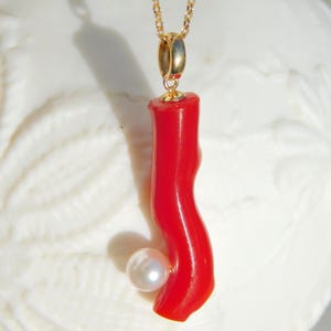 May include: A gold chain necklace with a red coral pendant and a white pearl accent.