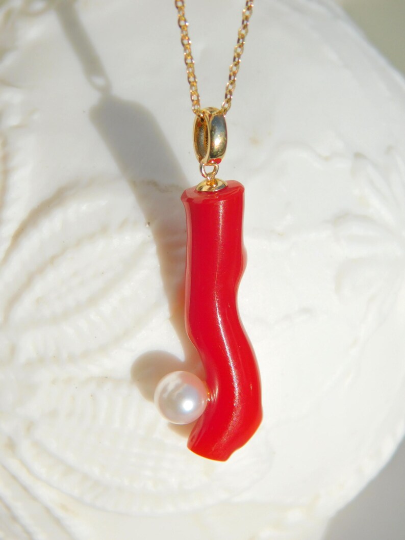 May include: A gold chain necklace with a red coral pendant and a white pearl accent.