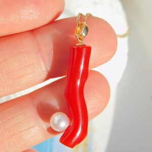 May include: A red coral pendant with a white pearl accent, hanging from a gold chain.