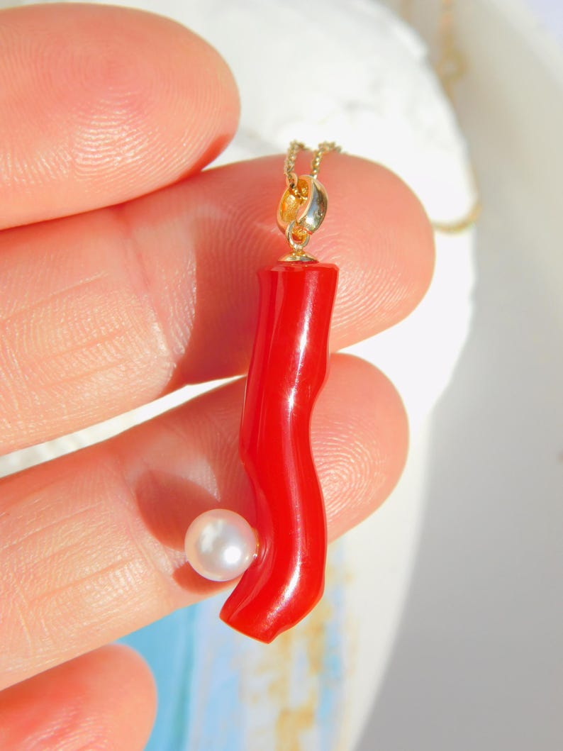May include: A red coral pendant with a white pearl accent, hanging from a gold chain.